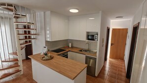 Una cocina moderna con armarios blancos, una isla de madera, microondas integrado y lavavajillas de acero inoxidable.