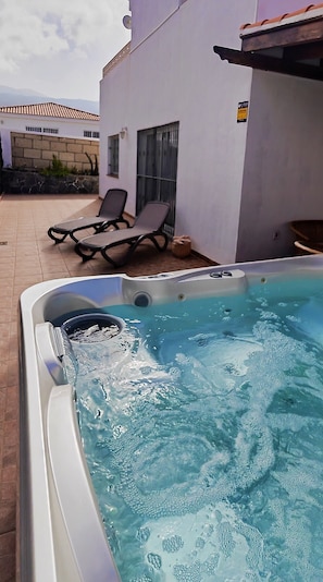 Un jacuzzi con agua, un patio con sillas y un edificio al fondo.