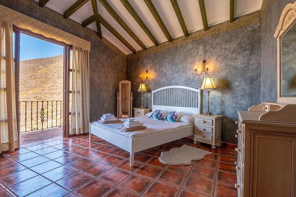 Una camera da letto con un letto, comodini, una cassettiera e vista su un paesaggio montuoso attraverso una porta scorrevole.