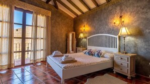 Une chambre à coucher avec un lit, des tables de chevet, un miroir et une fenêtre avec des rideaux.