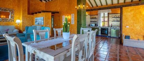 Een ruime woonkamer met een eettafel, stoelen en een keuken op de achtergrond.