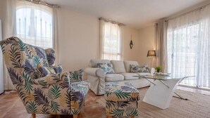 Una sala de estar con sofá, sillones, una mesa de centro de vidrio y una lámpara.
