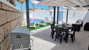 Un patio con una parrilla, mobiliario exterior y una piscina.