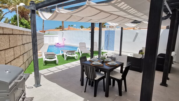 Un patio con una parrilla, una mesa de comedor, sillas y una piscina con un flotador de flamenco.