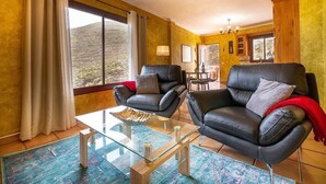 Une pièce avec deux canapés en cuir noir, une table basse en verre et une vue sur un paysage montagneux grâce à de grandes fenêtres.