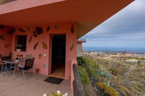 A pink building with a patio area, a table with chairs, and a view of the landscape. - Apartamento Vulcano - Two Bedroom Apartment, Sleeps 3 (Adeje)