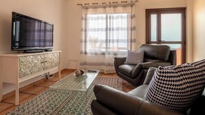 Un salon avec un téléviseur, un canapé en cuir, un tapis à motifs et une fenêtre avec des rideaux.