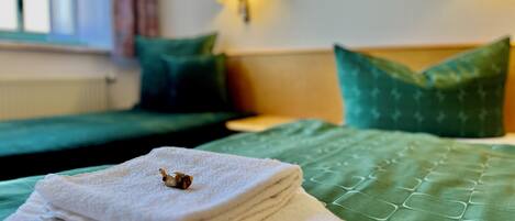 A neatly made bed with green bedding and a folded white towel with a small decorative item on top.