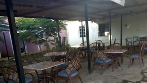 Een terras buiten met stenen vloer en houten tafels en stoelen.