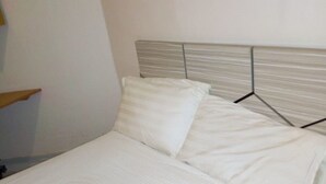 Een keurig opgemaakt bed met witte lakens en een houten hoofdeinde.