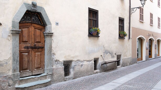Un edificio histórico con una gran puerta de madera, un arco de piedra y una calle adoquinada.