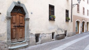 Un edificio histórico con una puerta de madera grande, un arco de piedra y un pequeño ventanal con flores.