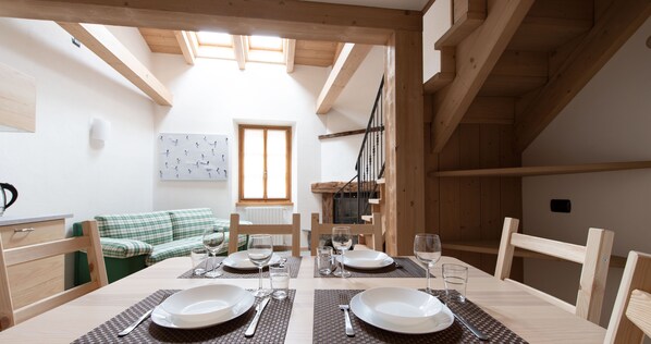 A dining area with a wooden table set for two, a green sofa, and a staircase. - Italianway - Roma 39 Mansarda (Bormio)