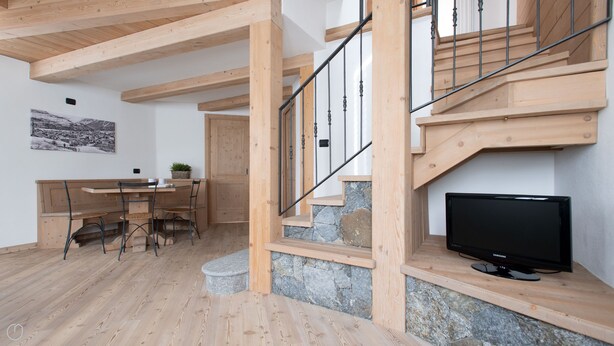 A wooden interior with a staircase, a dining area, and a TV on a wooden shelf. - Italianway - Roma 39 (Bormio)