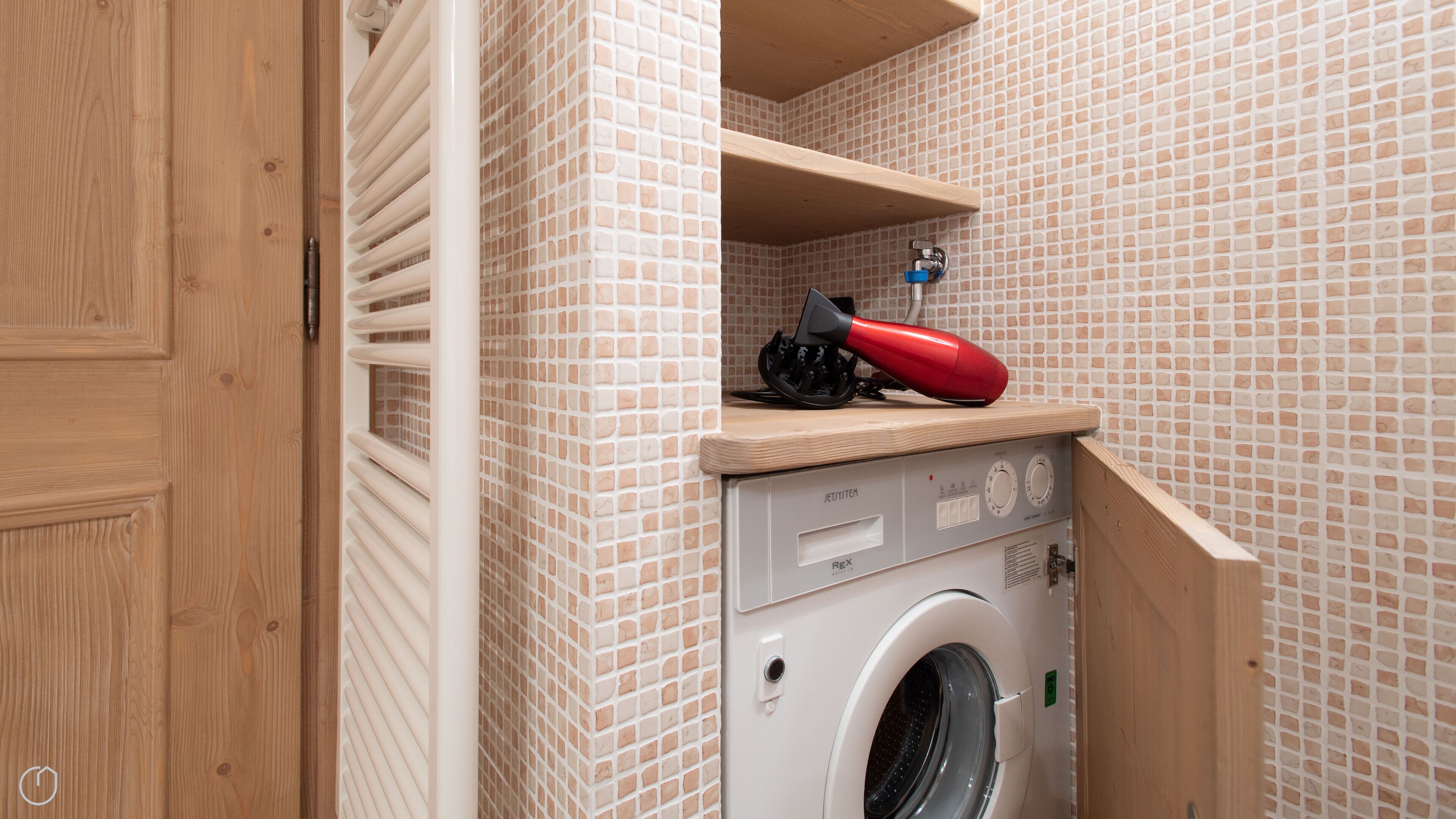 A compact laundry room with a washing machine, a drying rack, and a red hairdryer on a shelf.