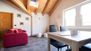 Um quarto acolhedor com teto de madeira, um sofá vermelho, uma mesa com cadeiras e uma janela com persianas.