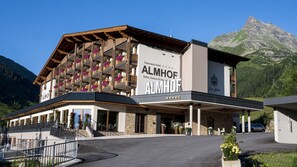 Un hotel con fachada de madera, balcones adornados con flores y vistas a la montaña.