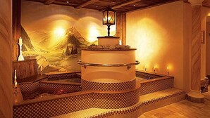 Un área de spa con una bañera de hidromasaje central, escalones con mosaicos, vigas de madera y un mural de montaña.