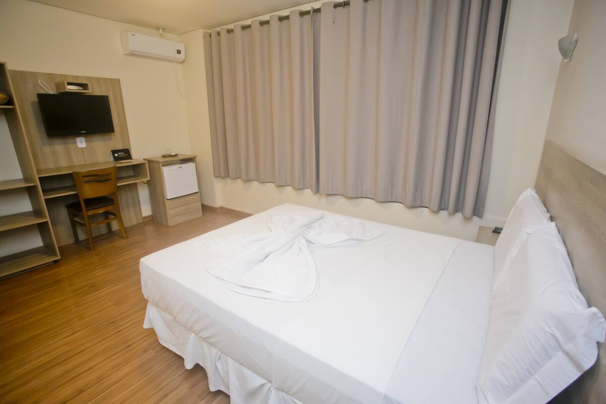 A hotel room with a bed, a desk, a chair, a television, and a window with curtains.