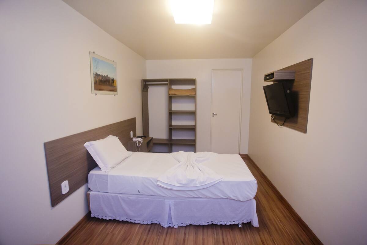 A neatly arranged bedroom with a bed, a bedside table, a TV mounted on the wall, and a door leading to a closet.