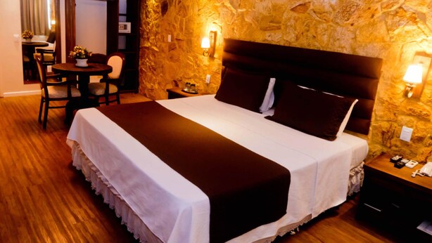 A hotel room with a large bed, a wooden floor, a stone wall, a small table with a chair, and a desk with a chair. - Dallé Hotel (Bage)