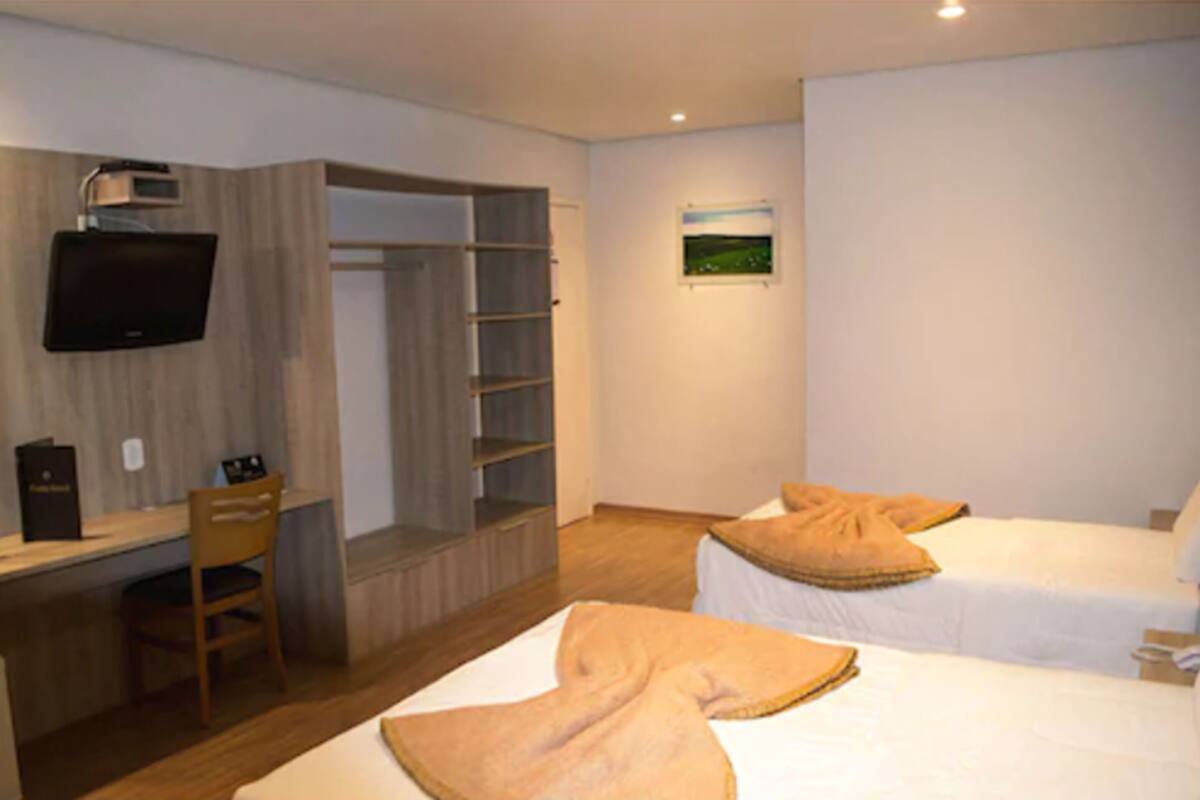 A hotel room with two beds, a desk with a chair, a TV mounted on the wall, and a wardrobe.