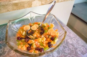 Un tazón de vidrio con una ensalada de frutas y una cuchara.