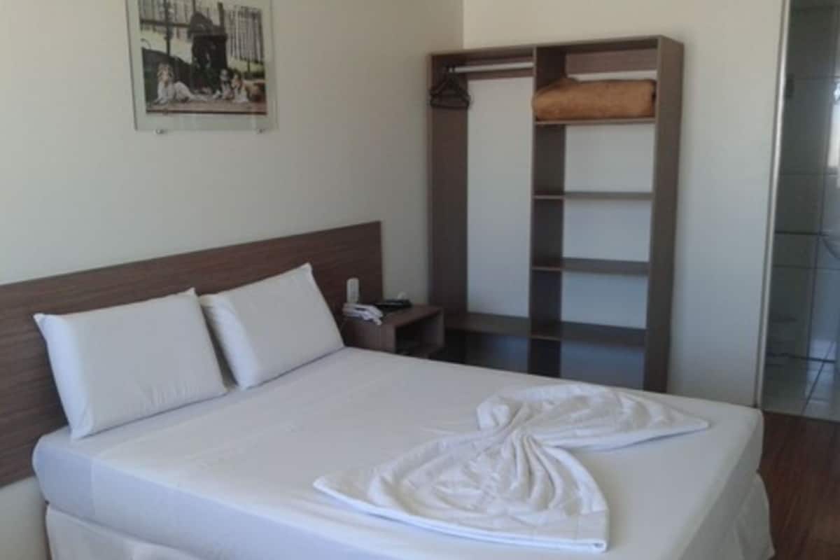 A neatly made bed with white linens, a wooden headboard, a bedside table with a lamp, and a large wardrobe.