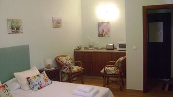 Una habitación de hotel con cama, dos sillas, un escritorio con computadora y una pequeña kitchenette.