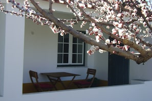 Un bâtiment blanc avec une fenêtre et une table entourée de chaises à l’extérieur.