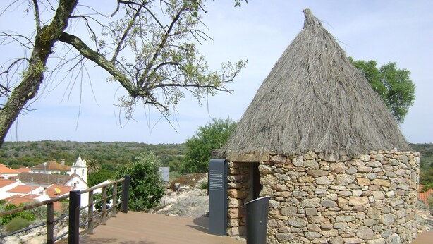 Eine traditionelle Steinhütte mit einem Reetdach, einer hölzernen Bank und einer Steinmauer.