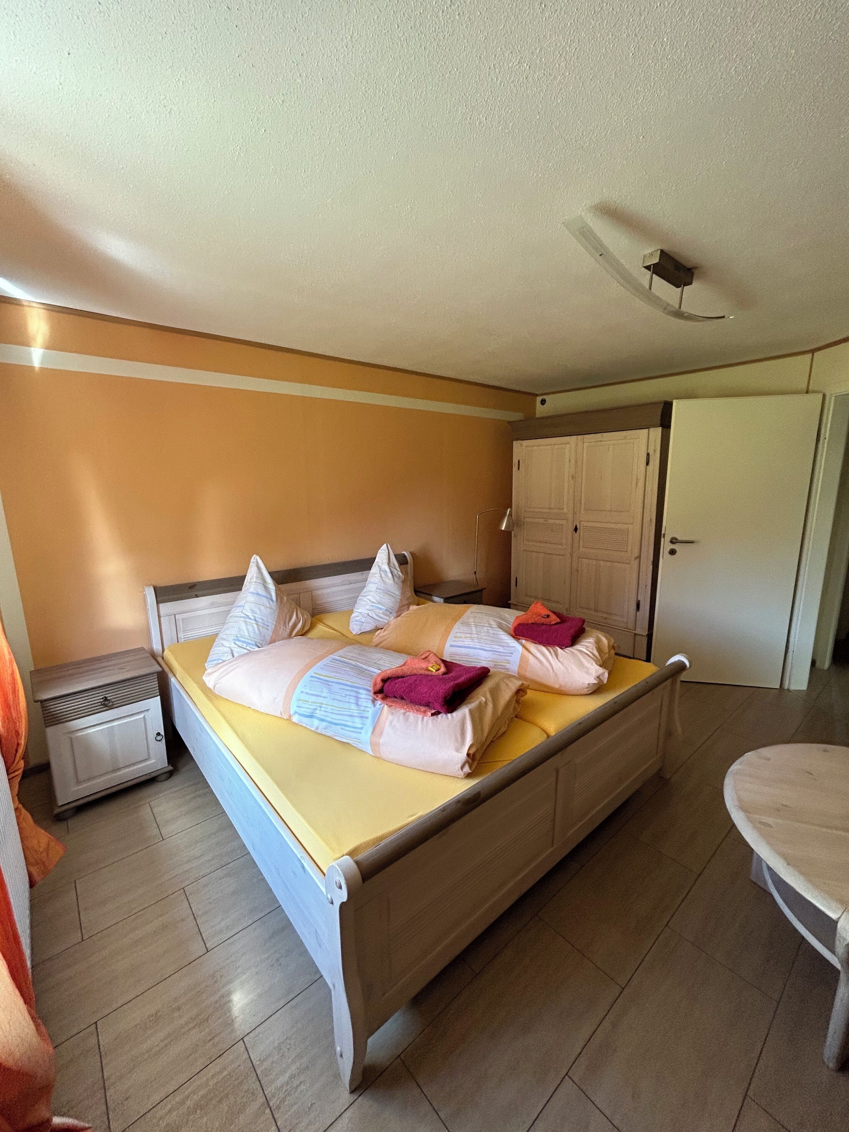 Une chambre d’hôtel avec un lit en bois, une table de chevet, un radiateur et une armoire.
