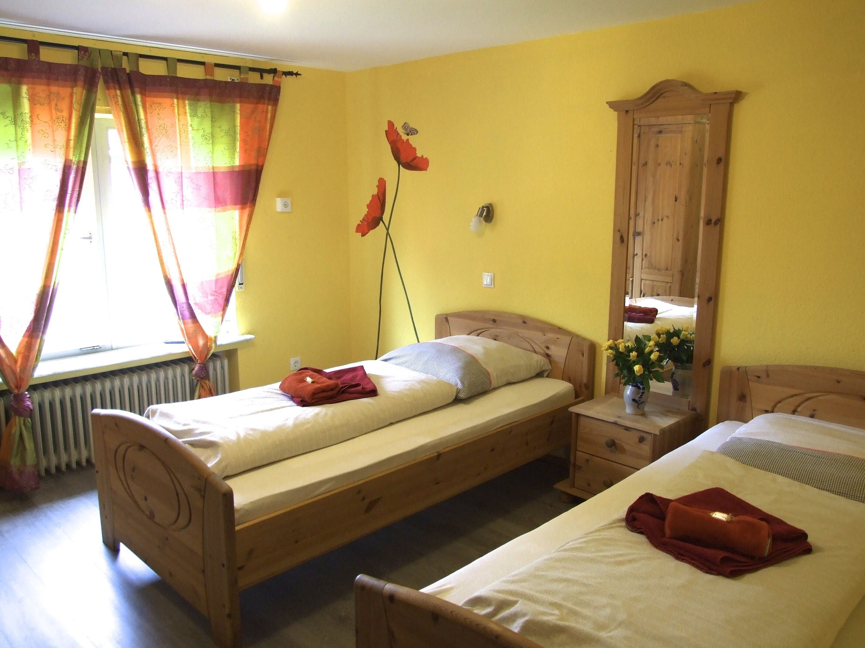 A room with two wooden beds, a wooden wardrobe, a radiator, and a window with colorful curtains.