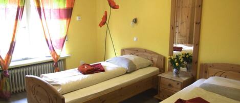 A room with two wooden beds, a wooden wardrobe, a radiator, and a window with colorful curtains.