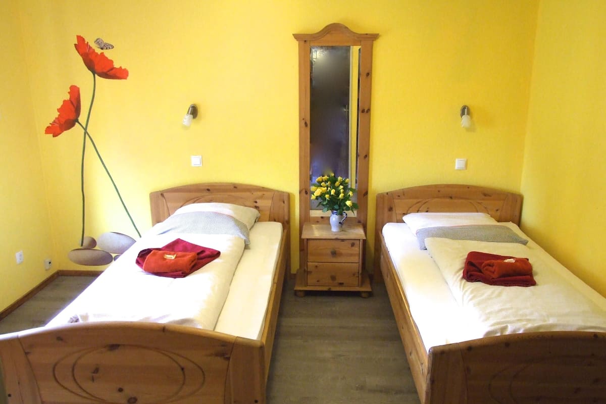 A room with two wooden beds, a wooden nightstand with a mirror, and a vase with flowers.