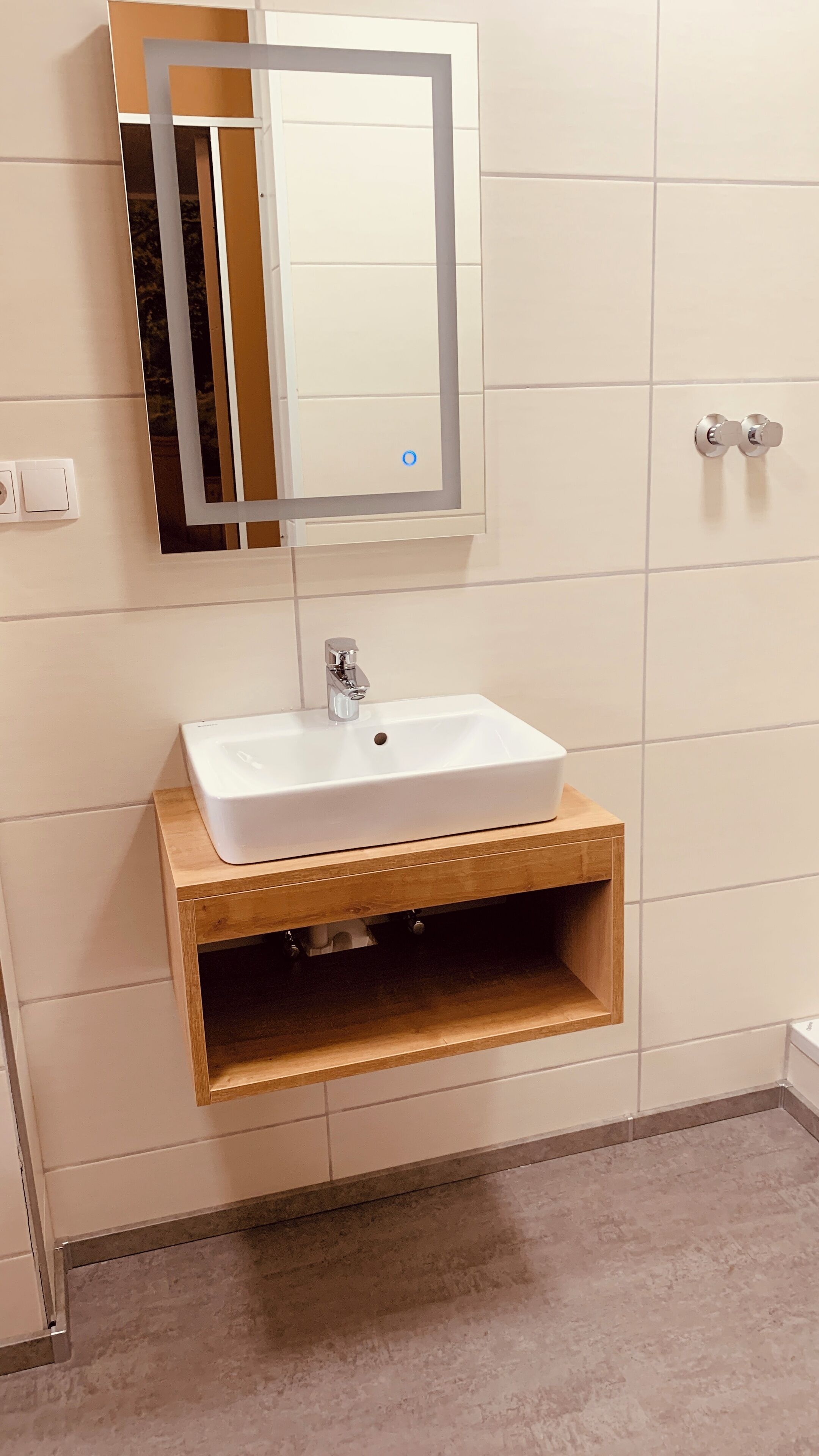 A bathroom with a white sink, wooden vanity, and a mirror with a silver frame.
