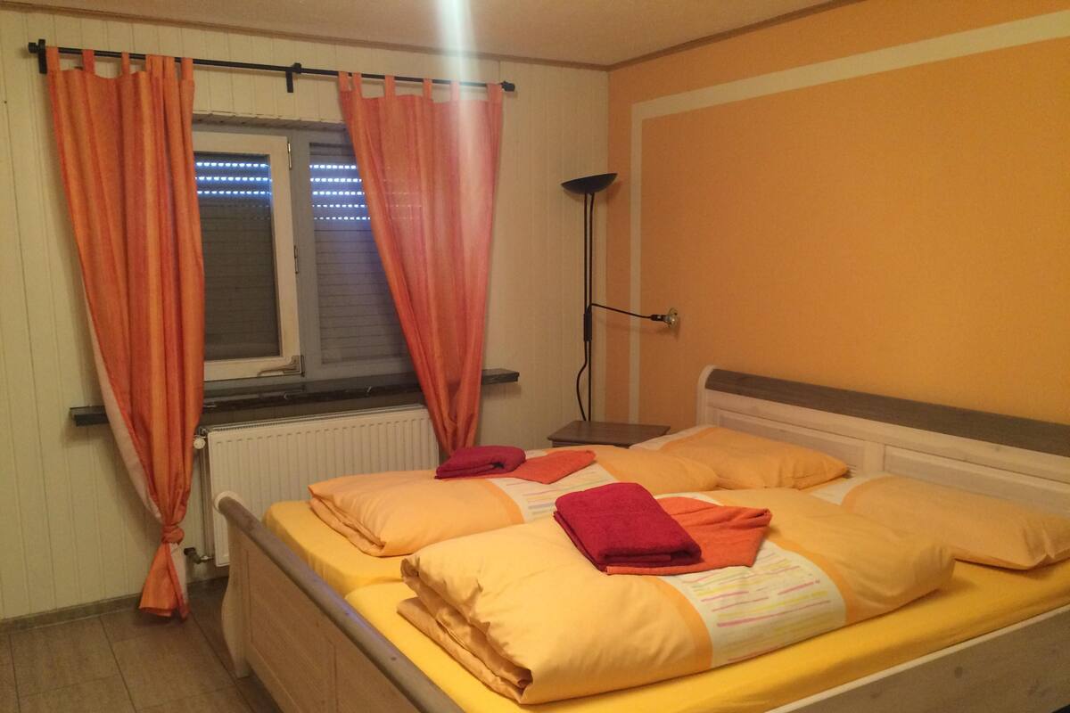 A single bed with yellow bedding, a nightstand with a lamp, and orange curtains.