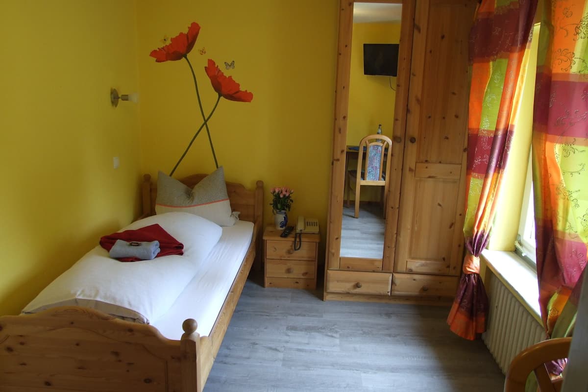 A bedroom with a wooden bed, a nightstand, a mirror, and a window with curtains.