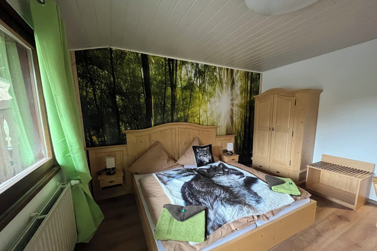 A bedroom with a bed, a nightstand, a wardrobe, and a window with green curtains.