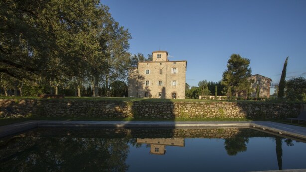Un edificio de piedra con su reflejo en aguas tranquilas, rodeado de árboles y vegetación.