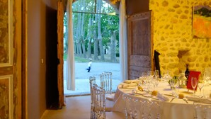 Un comedor interior con vistas a árboles a través de un ventanal, una pared de piedra y una mesa dispuesta para una comida.