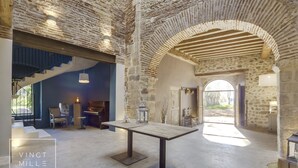 Una habitación amplia con una pared de piedra rústica, una mesa de madera y una escalera que sube a otro nivel.