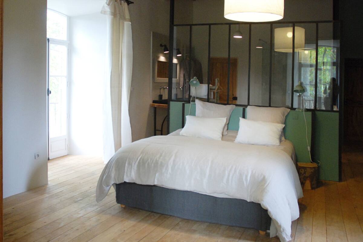 A bedroom with a large bed, a wooden floor, a green accent wall, and a window with curtains.