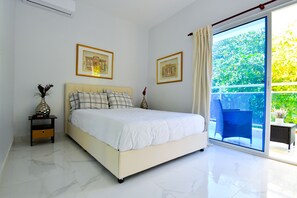 A bedroom with a bed, a nightstand, a window with a view of greenery, and two framed pictures on the wall.