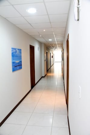 A long, narrow hallway with white walls, a tiled floor, and doors on both sides. - Miotto Executive Hotel (Navegantes)