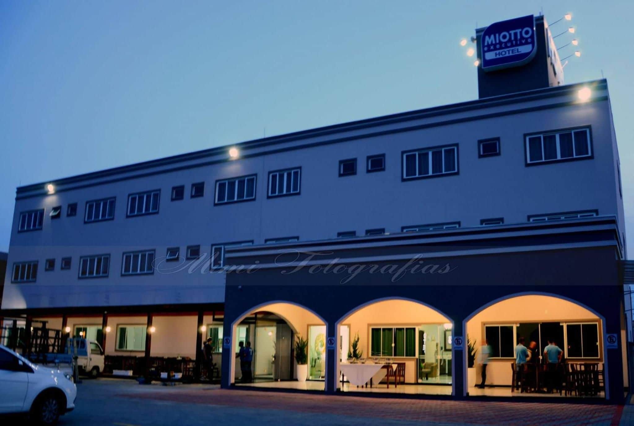 A hotel with a sign for 'MOTTO Executive Hotel' and a storefront named 'Mie Fotografias' with an entrance and outdoor seating.