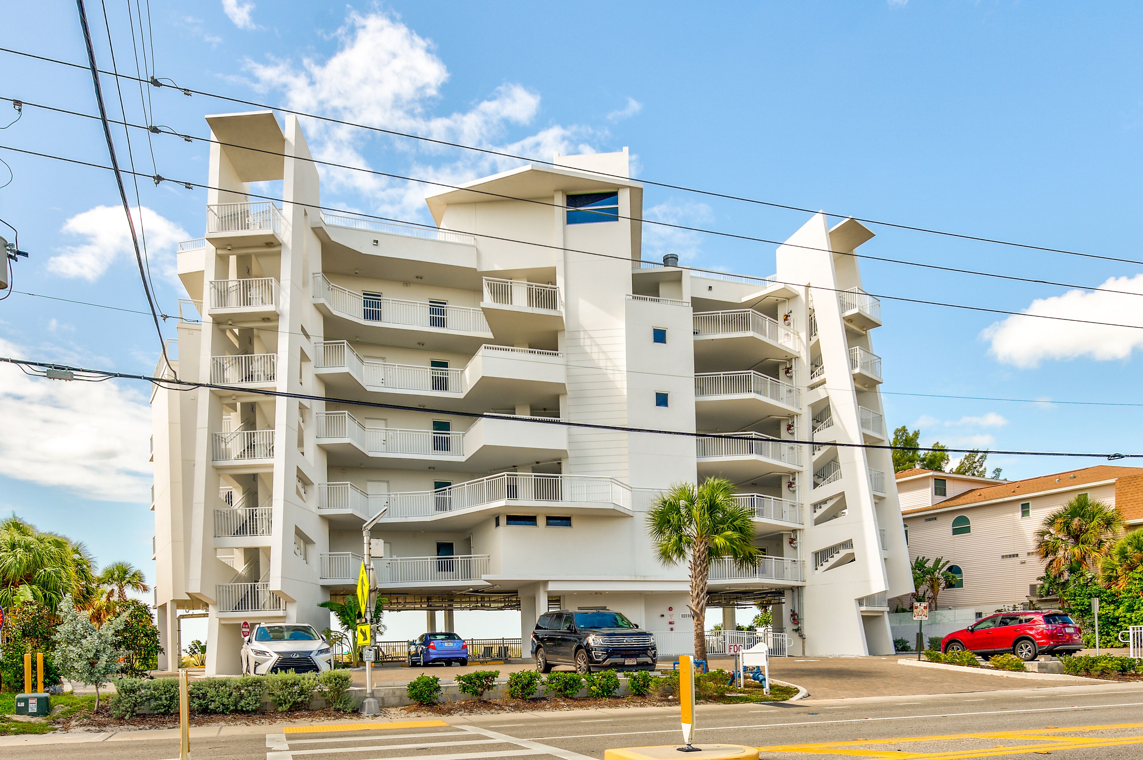 A multi-story residential building with balconies, parking spaces, and a clear sky.