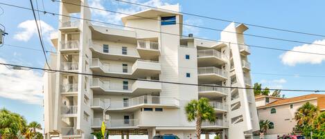 A multi-story residential building with balconies, parking spaces, and a clear sky.