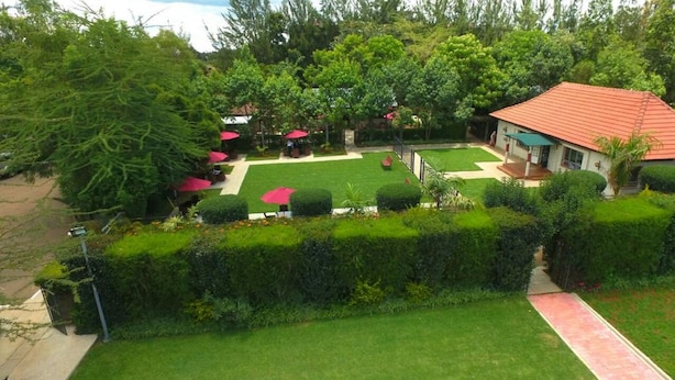 A well-maintained garden with a lawn, hedges, and a small pavilion with red umbrellas. - The Noble Hotel and Conference Center (Eldoret)