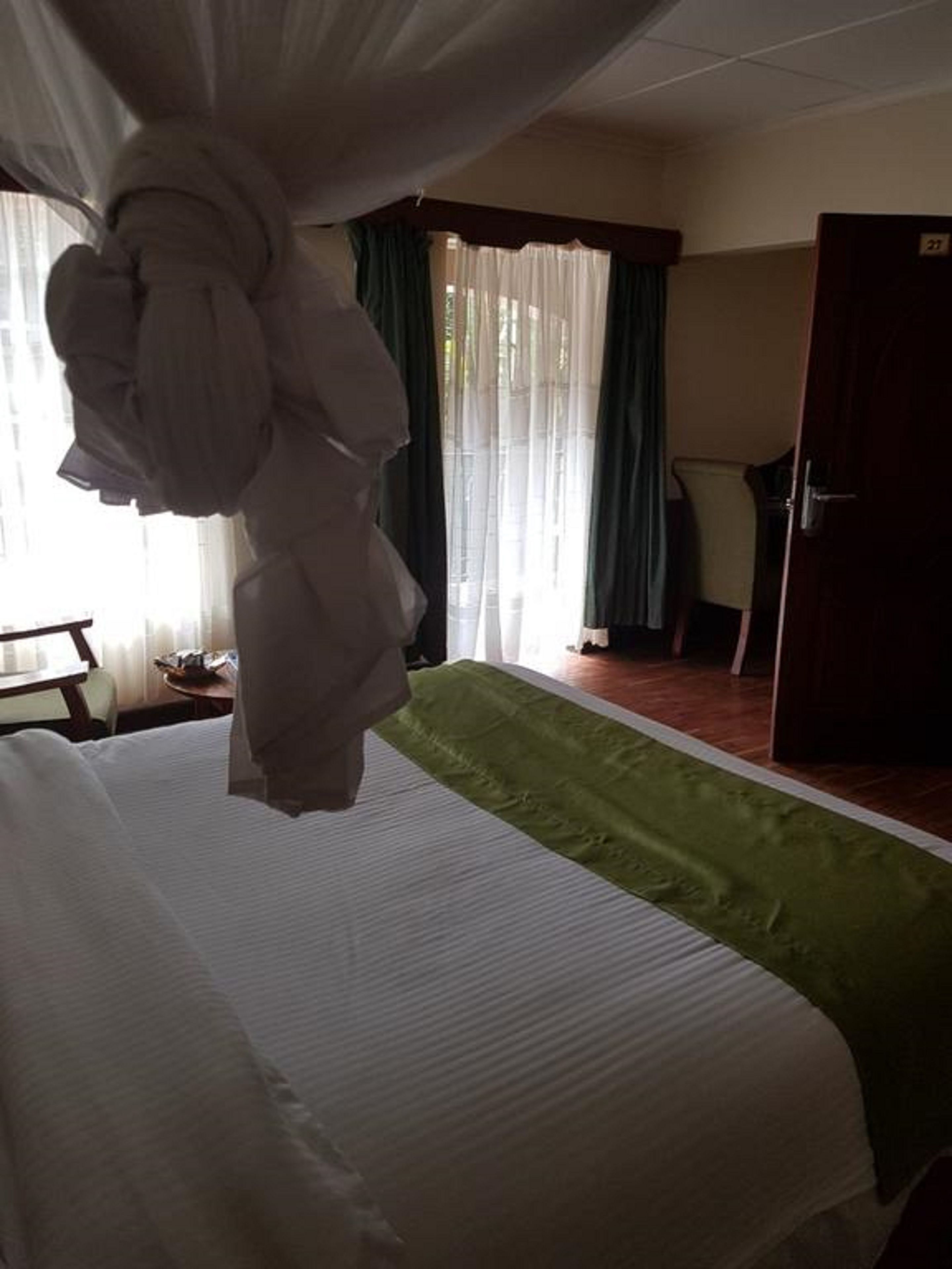 A hotel room with a bed, a green bedspread, a chair, a desk, and a door.